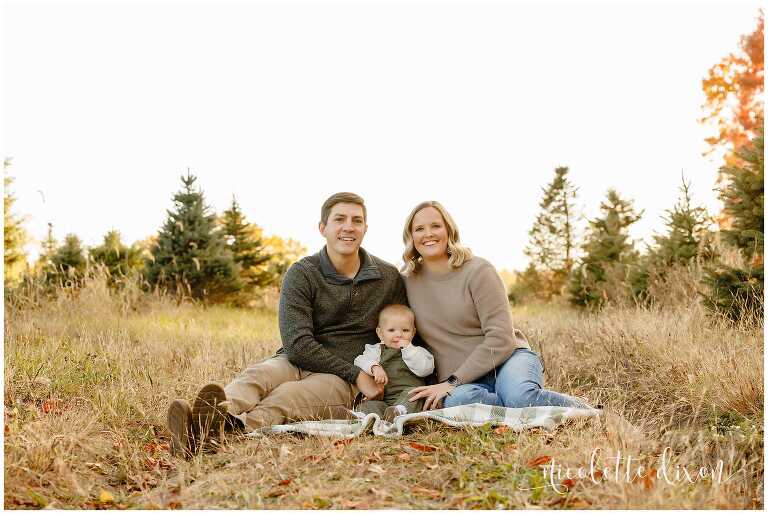 Family with one year old baby boy sitting in grass at Aliison's Christmas Tree Farm near Pittsburgh PA