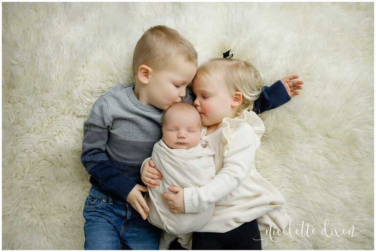 Brother and sister kissing newborn brother in studio in North Fayette Township near Pittsburgh.